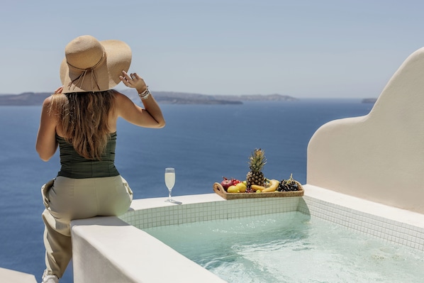 Eine Person sitzt am Pool mit Blick aufs Meer, eine Obstkorb und ein Glas Wasser.