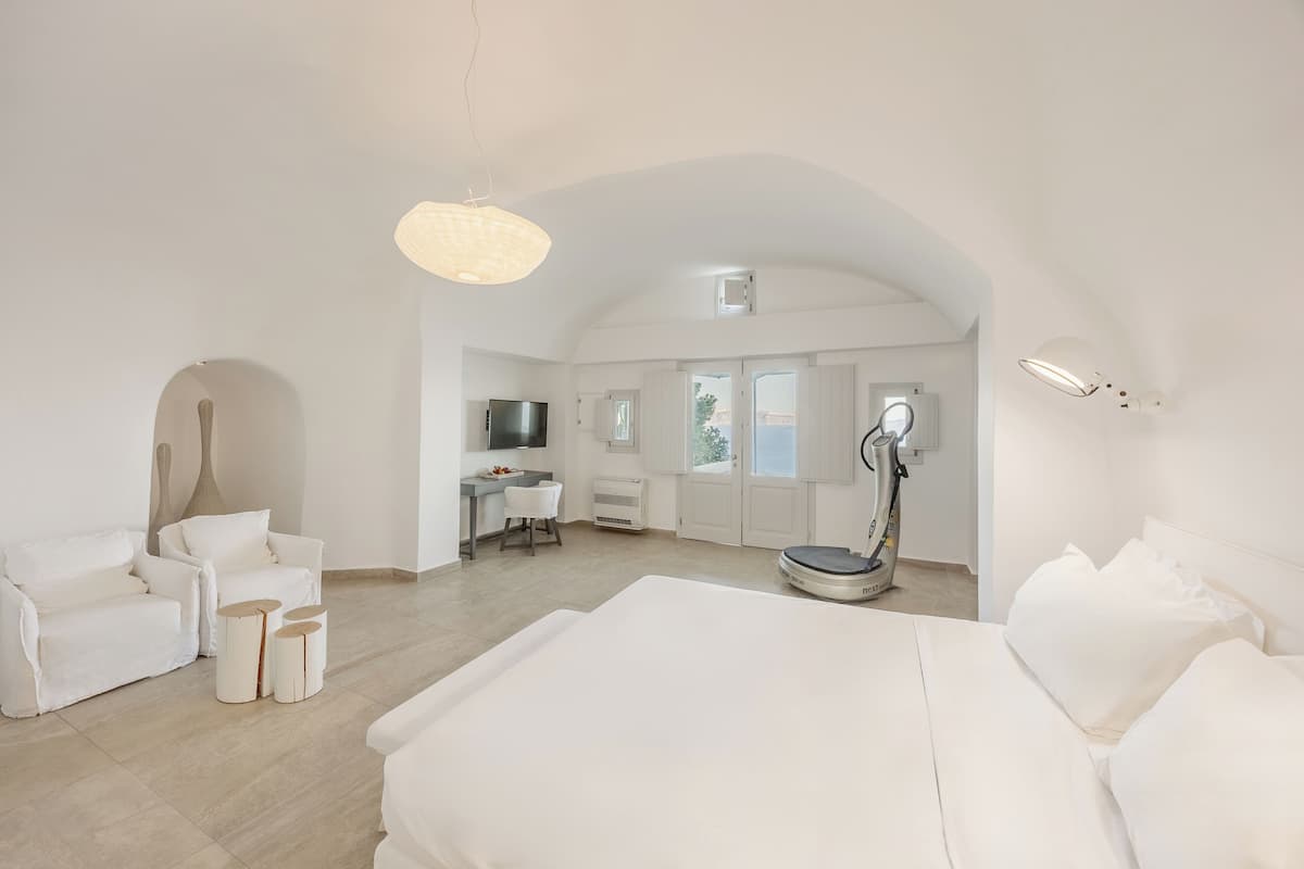 Ein geräumiges Schlafzimmer mit einem großen Bett, einem Schreibtisch und einem Stuhl, ein Badezimmer mit Toilette und Dusche sowie eine Wohnbereich mit Sofa und Lampe.