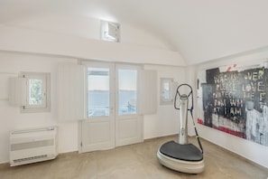 Ein Zimmer mit Meerblick, einem Standventilator und einem großen abstrakten Gemälde an der Wand.