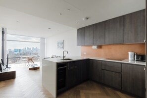 Eine moderne Küche mit dunklen Holzschränken, einer Edelstahlspüle und Blick auf die Stadt durch große Fenster.