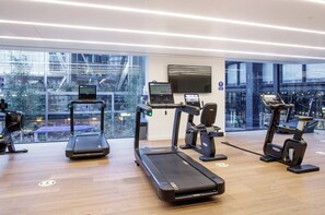 Ein modernes Fitnessstudio mit Laufbändern, Ergometer und Rudergerät, ausgestattet mit großen Fenstern und Blick auf die Stadt.