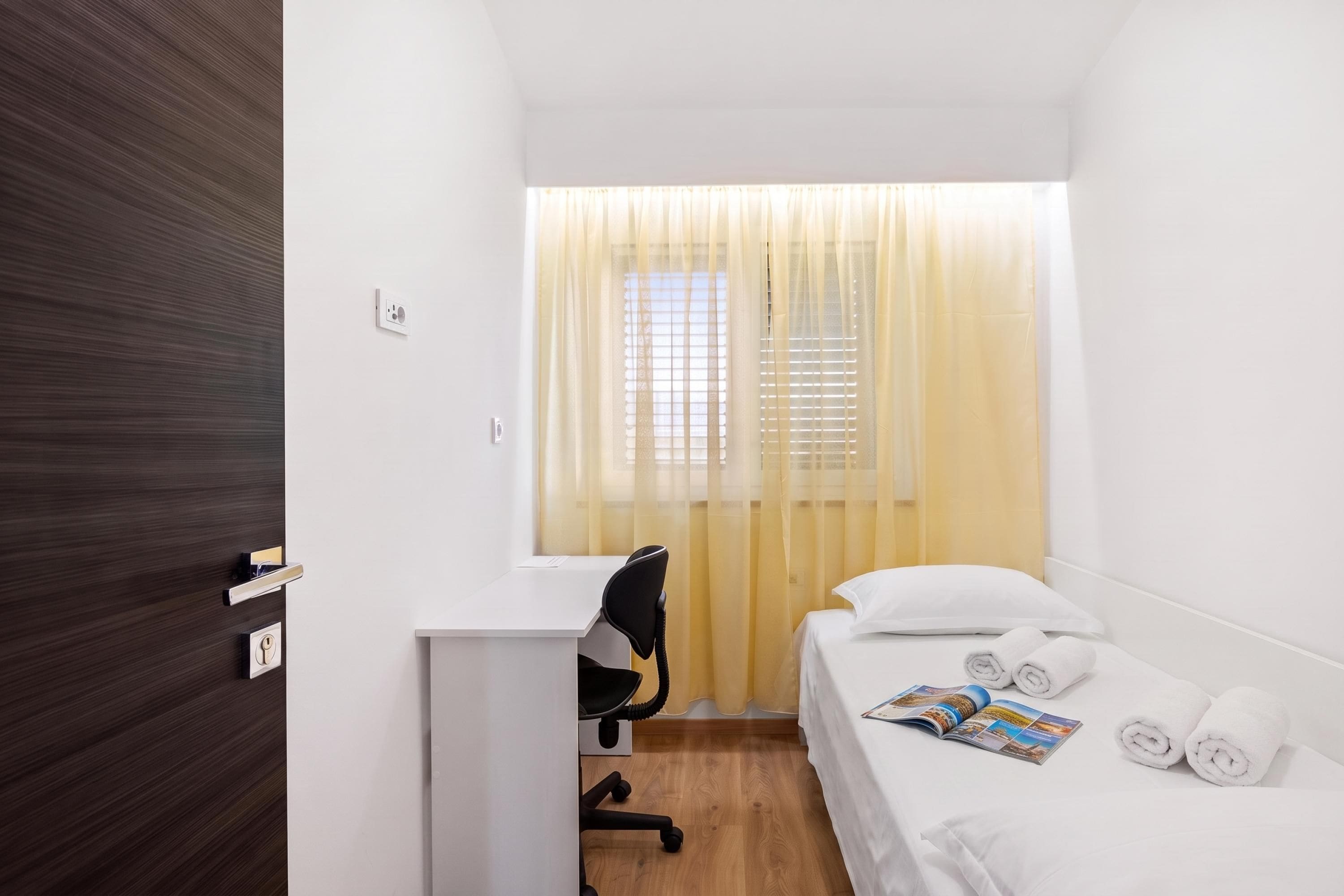 Une petite chambre d’hôtel, bien aménagée et comprenant un lit, un bureau et une chaise.