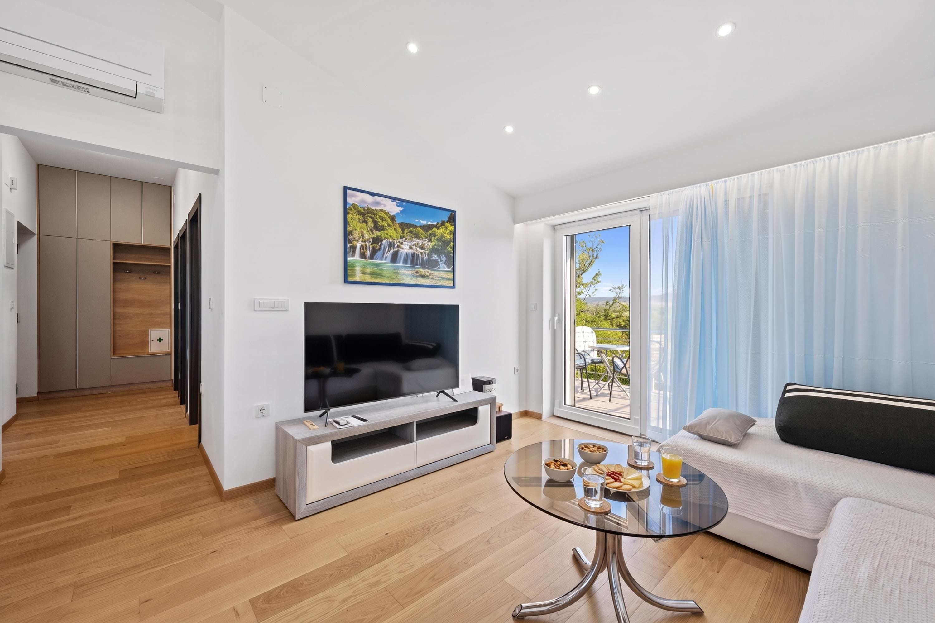 A modern living room with a flat-screen TV, a glass coffee table, and a sofa.