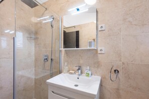 Ein modernes Badezimmer mit einer gläsernen Duschkabine, einem weißen Waschbecken und einem Spiegel darüber.