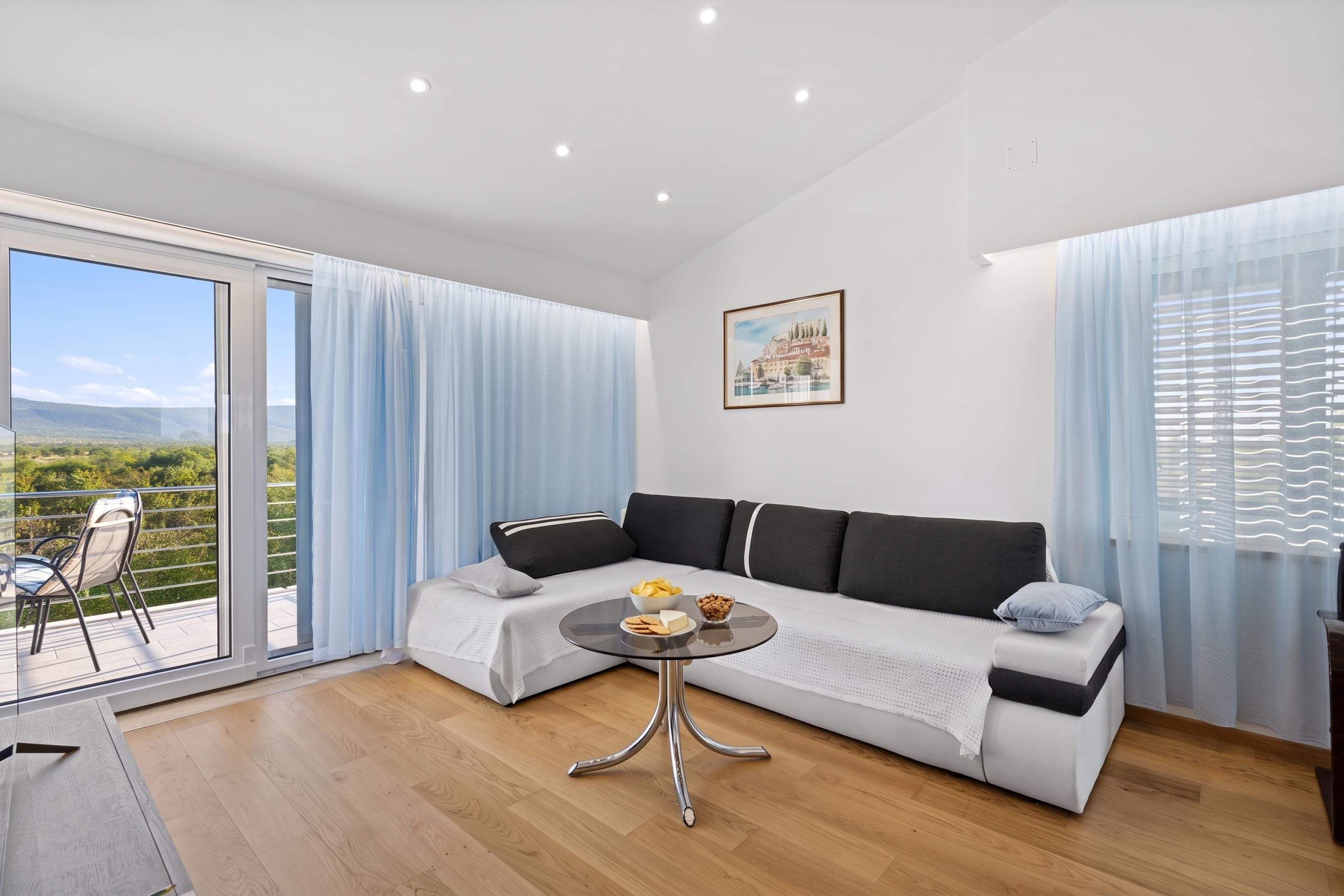 A modern living room with a sofa, a glass coffee table, and a balcony with a view.