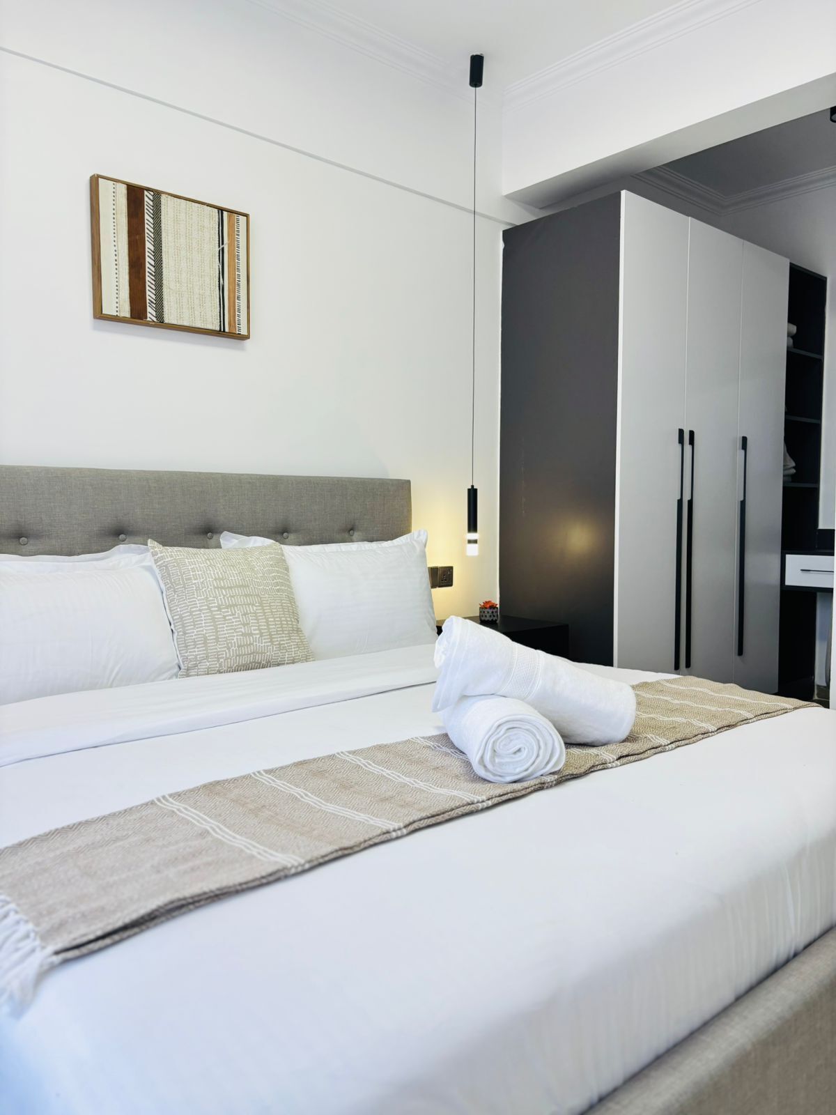 Una cama bien hecha con una toalla enrollada, un cabecero, una obra de arte en la pared y un armario.