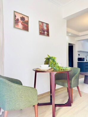 Un comedor con una mesa redonda, dos sillas, una planta en maceta y dos cuadros en la pared.