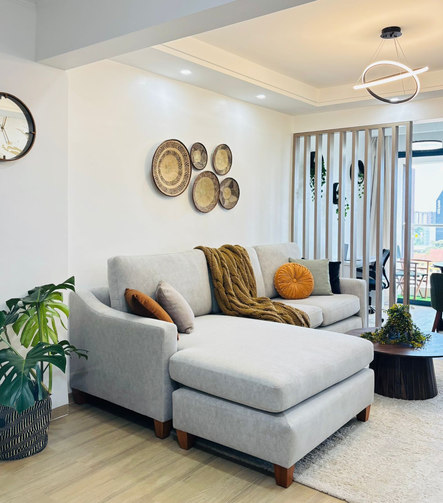 Una sala de estar moderna con un sofá seccional gris, un reloj de pared redondo y decoración mural.