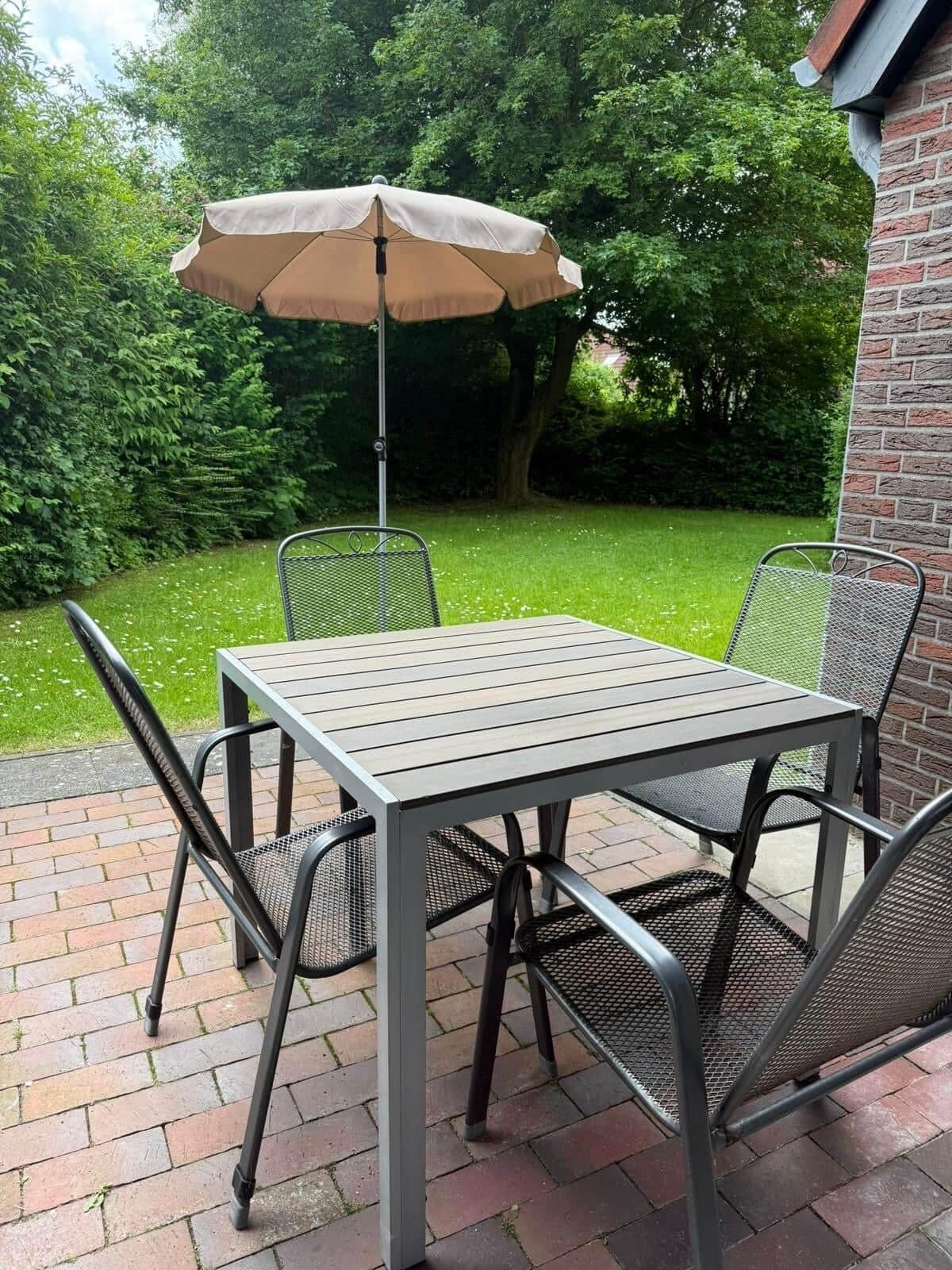 Eine Terrasse im Freien mit Tisch und Stühlen, einem Sonnenschirm und einer Backsteinmauer.