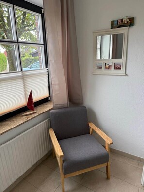 Ett hörnrum med ett fönster, ett element, en stol och en vägghylla med bilder.