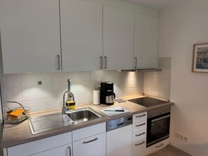 Eine moderne Küche mit weißen Schränken, einer Edelstahlspüle, einer Kaffeemaschine und einem Geschirrspüler.