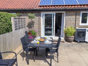 Eine Terrasse im Freien mit Frühstückstisch, Holzlattenzaun und Solaranlage auf dem Dach.