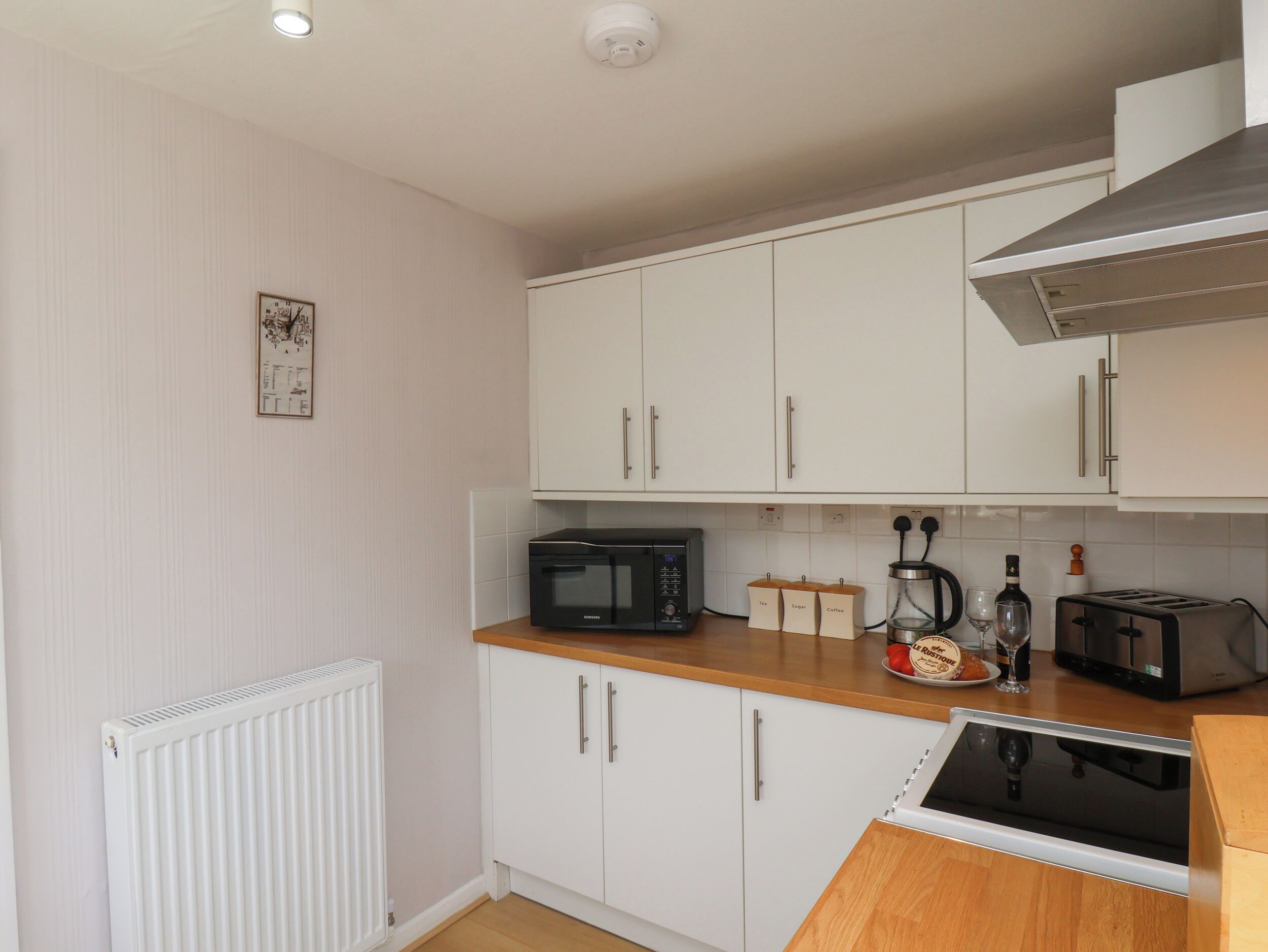 A compact kitchen with white cabinets, a microwave, a toaster, and a kettle.