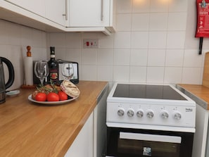Eine Küche mit einem weißen Herd, einem Toaster, einem Teller mit Tomaten und Brot sowie einer Weinflasche.