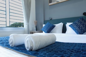 Een net opgemaakt bed met blauw-wit beddengoed, een geborduurde blauwe matras en een raam met zonwering.