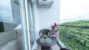 En balkon med fletmøbler, et glasbord og en potteplante.