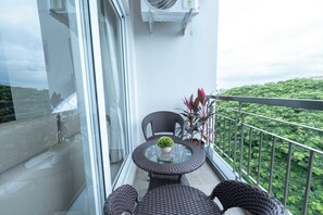 Een balkon met rieten meubels, een glazen tafel en een potplant.