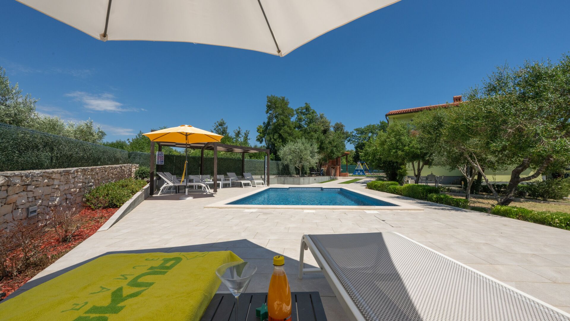 Ein Poolbereich mit Liegestühlen, einer Pergola mit Sonnenschirm und einem kleinen Pool.