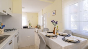 Une cuisine compacte équipée d’une cuisinière à gaz, de meubles blancs et d’un coin repas avec une table dressée pour deux personnes.