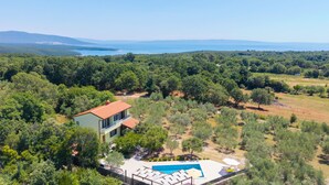 Une maison à deux étages avec une piscine, entourée d’une végétation luxuriante et offrant une vue sur la mer.