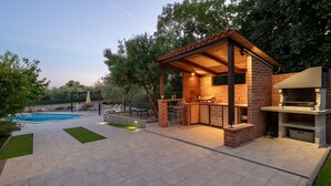 Un espace cuisine extérieur doté d’une structure en briques, d’une piscine et d’une pergola.