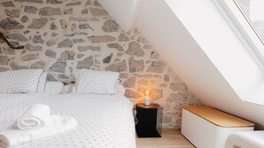 Ein Schlafzimmer mit Stehwand, einem Bett mit weißer Bettdecke, einem Nachttisch mit Kerze und einer Bank.