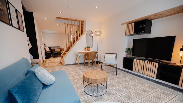 Ein Wohnzimmer mit Sofa, Fernseher, Essbereich und einer Treppe.