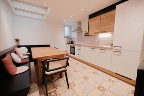 A modern kitchen with a wooden table and chairs, white cabinets, and a patterned floor. - 26 Pas de la Place (Gerpinnes)