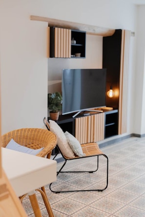 A modern living room with a flat-screen TV, wicker furniture, and a patterned floor. - 26 Pas de la Place (Gerpinnes)