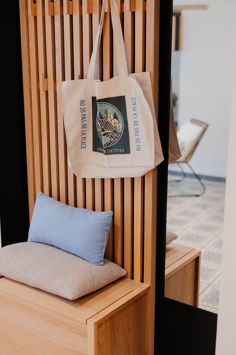 Un mur fait de lattes de bois, sur lequel est accroché un sac en toile beige orné d’un logo et d’un texte.