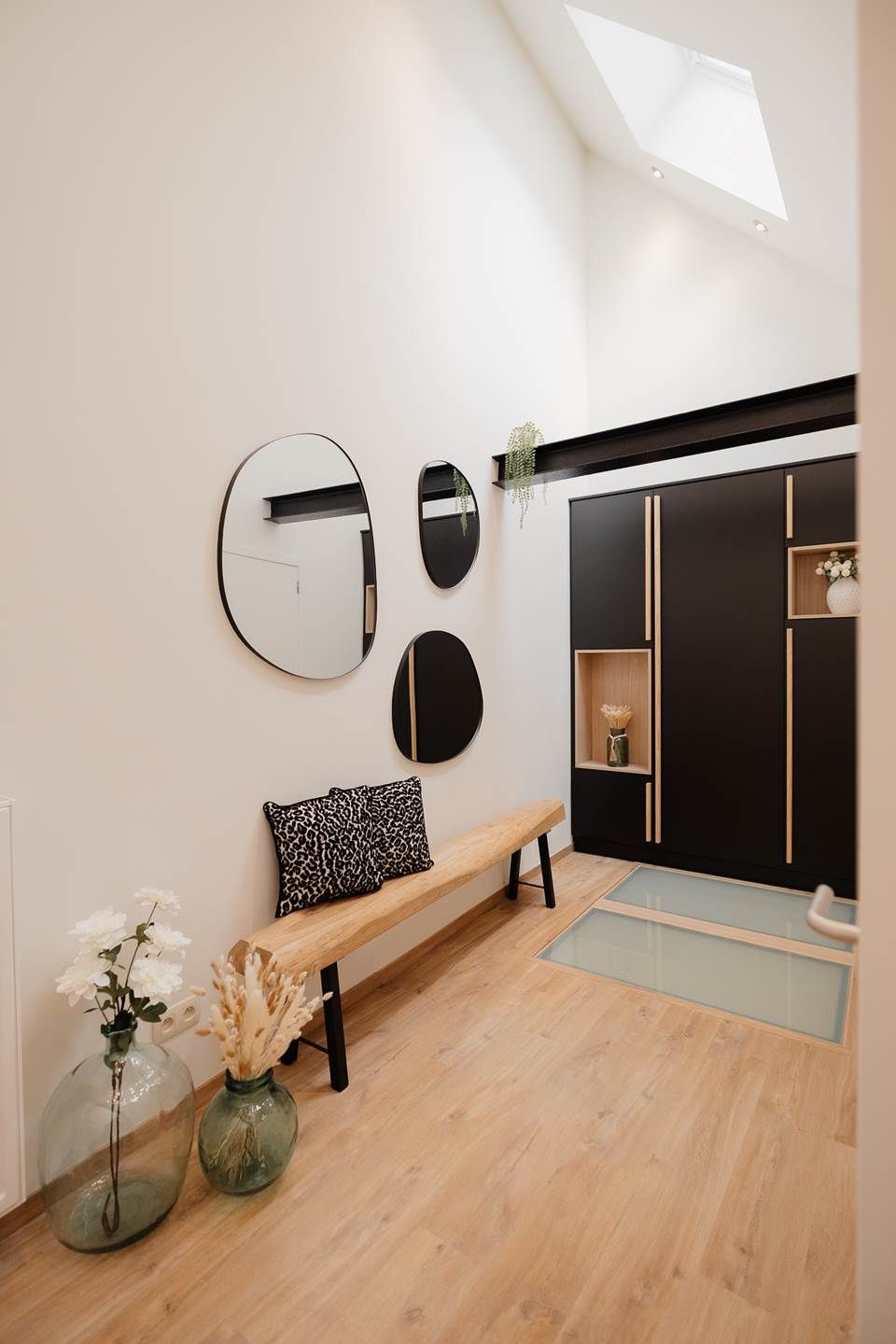 A modern interior with a bench, mirrors, and a black wardrobe.