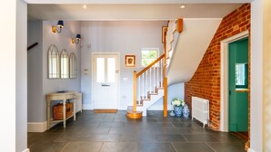 Un couloir avec un escalier, une porte, un radiateur et une table sur laquelle se trouvent des paniers.
