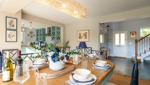 Un coin repas avec une table en bois dressée pour le repas, une cuisine en arrière-plan et un escalier menant à un autre niveau.