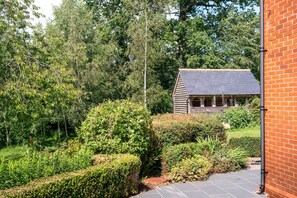 A house with a sloped roof, surrounded by dense greenery and a brick wall.