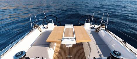 A boat deck with a central table, two steering wheels, and a view of the sea and distant land.