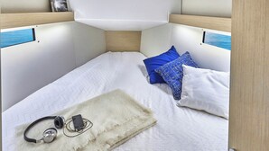 Habitación pequeña y luminosa con cama, almohadas, manta y auriculares.