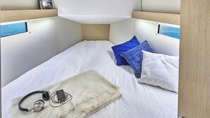 A compact, well-lit room with a bed, pillows, a blanket, and headphones. - Dubrovnik Delight: A Sun-Kissed Sailing Experience (Komolac)