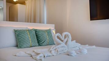 A hotel room with a neatly made bed, two green pillows, and a wall-mounted TV.