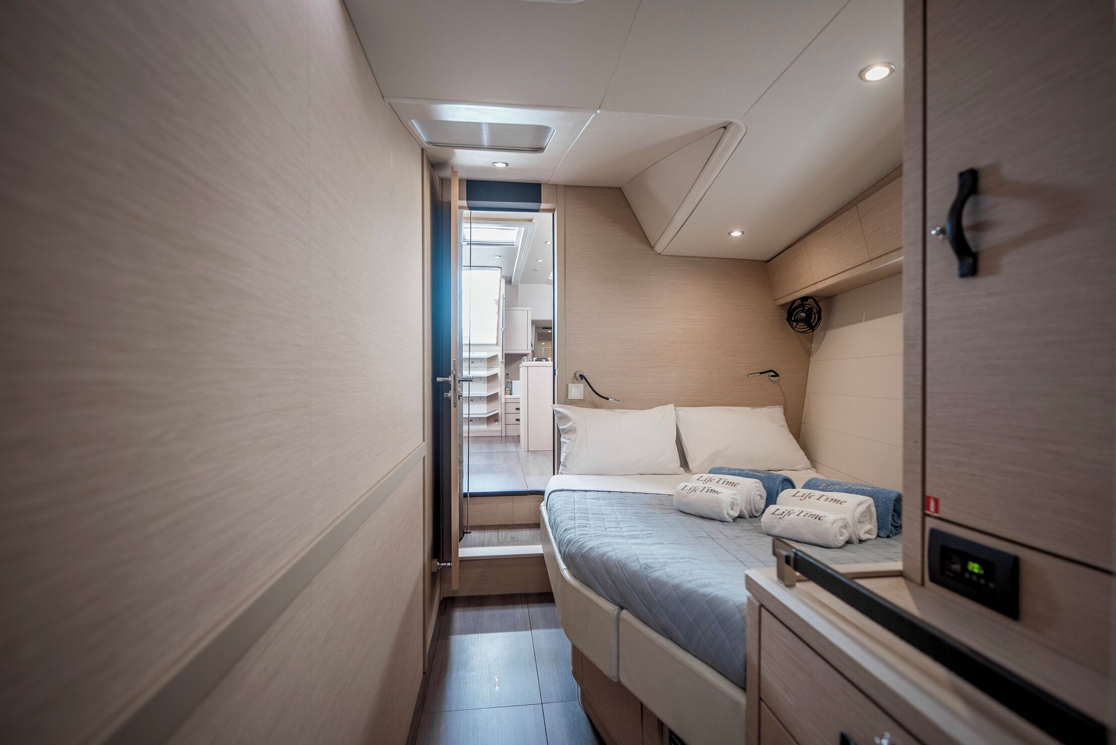 A narrow hallway leading to a bedroom with a bed, bedside tables, and a control panel.