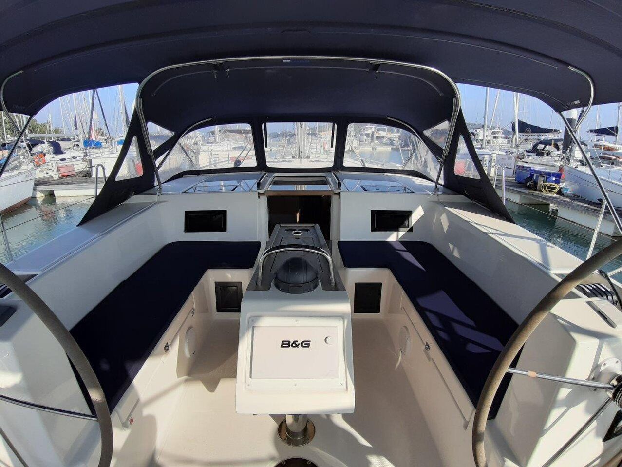 Het interieur van een boot met een B&G bedieningspaneel, een stuurwiel en uitzicht op de jachthaven.