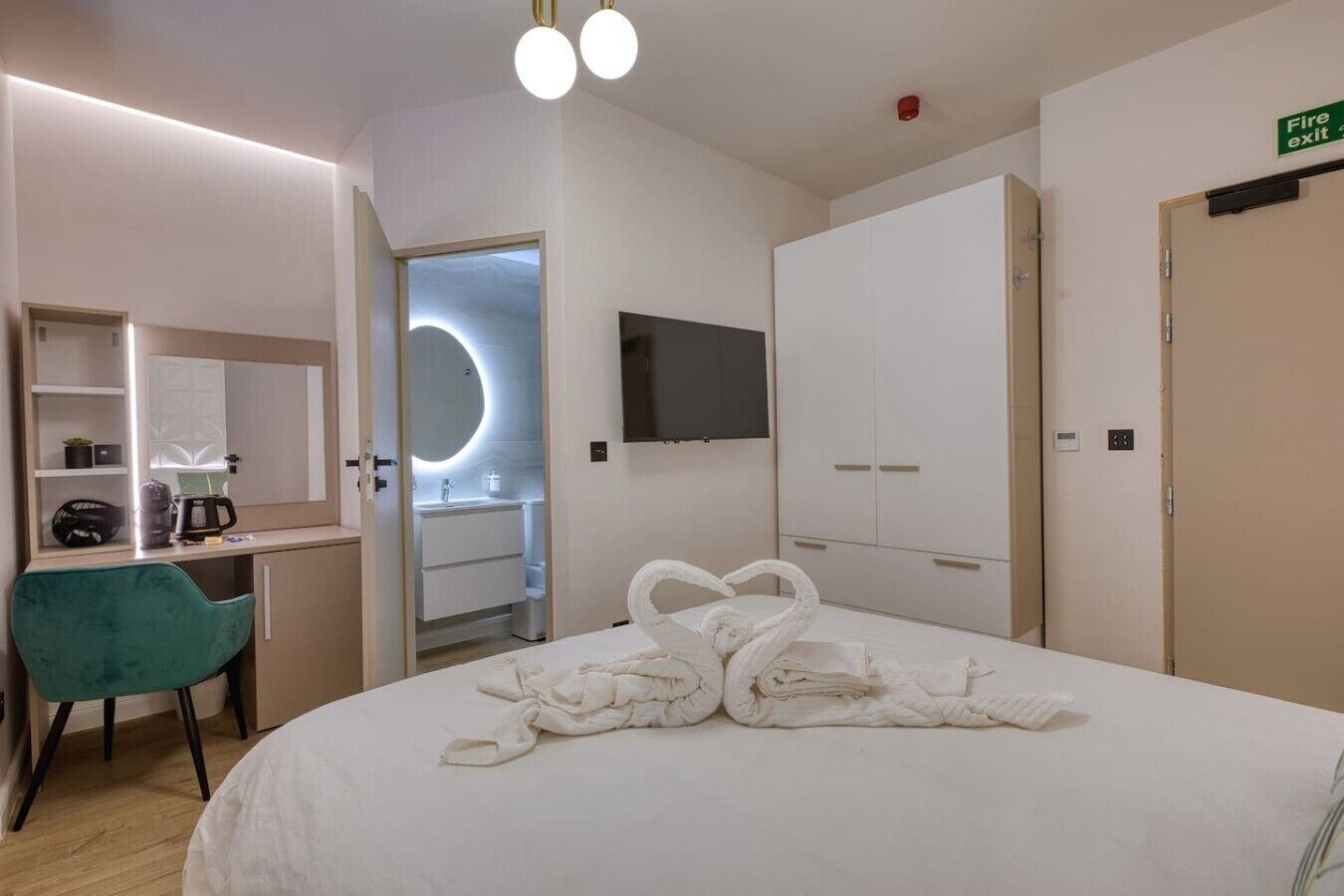A hotel room with a bed, a desk with a chair, a TV, a wardrobe, and a bathroom.