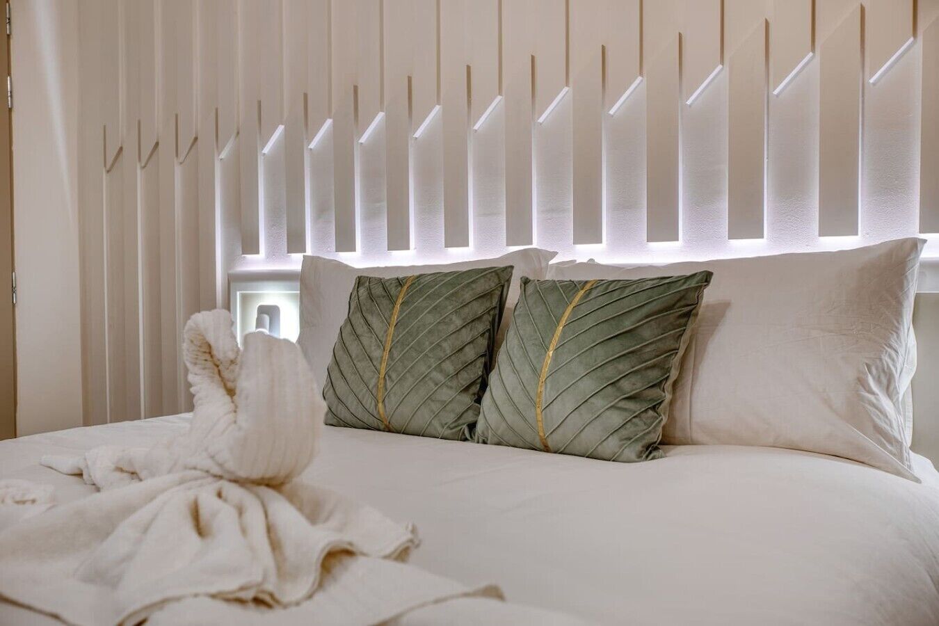 Un lit avec une literie blanche, deux oreillers verts ornés de bordures dorées et une serviette blanche posée sur le lit.