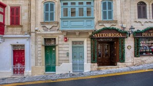 A building with a green door, a sign reading 'VITTORIOSA,' and a pharmacy sign. - 7 Main Gate - Double Room with Balcony (Birgu)