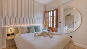 A hotel room with a bed, a wall-mounted mirror, and a door with an emergency exit sign. - 7 Main Gate - Double Room with Balcony (Birgu)