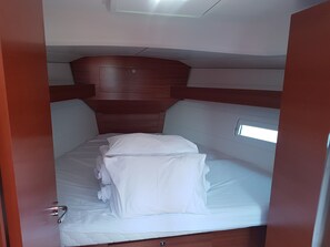 A compact, well-lit cabin with a single bed, a small window, and a wooden headboard.