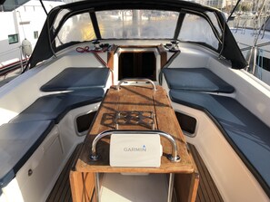 Le pont d’un bateau, avec une table en bois, un appareil de navigation Garmin et des espaces pour s’asseoir.
