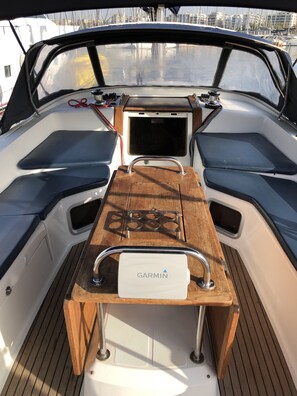 Convés de barco com dispositivo de navegação Garmin, mesa de madeira e áreas de estar.