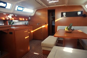 A compact kitchen with wooden cabinets, a countertop, and a sink. There is a small seating area with a table and a bowl of fruit. - Sun-Kissed Sailing Adventure in Islas Sarónicas (Alimos)