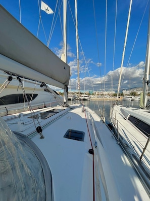 A marina with multiple sailboats docked, a clear sky, and a distant cityscape. - Sun-Kissed Sailing Adventure in Islas Sarónicas (Alimos)