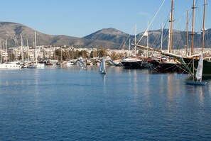 Ein Yachthafen mit Segelbooten, ein Segelboot mit einer Person an Bord und eine Stadtansicht mit Bergen im Hintergrund.